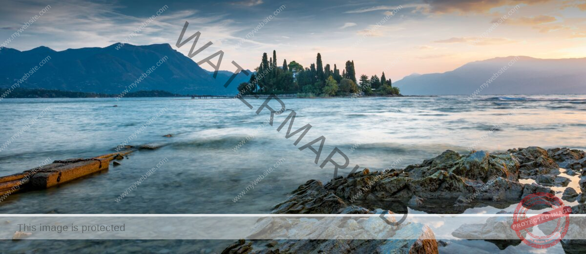 View of a sea with a small island full of tree in the middle with the mountains in the background